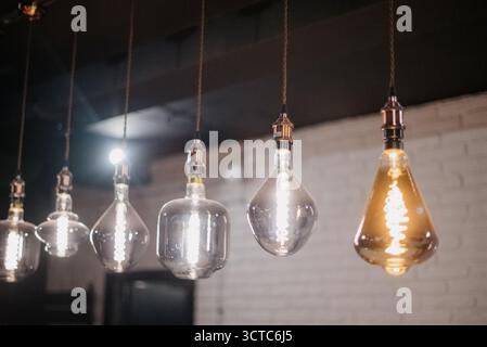 A row of vintage Edison pendant lamps in various shapes with warm and cool lighting. Decorative glowing incandescent light bulbs in a modern loft cafe Stock Photo