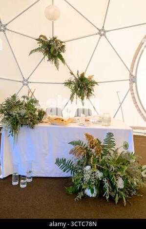 Wedding table decorated with natural plants and dried flowers in a white tent. A wedding table with eco-friendly decor made of greenery and ferns Stock Photo