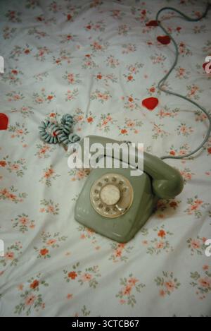 A vintage rotary telephone rests on a floral bedspread Stock Photo