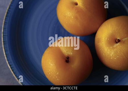 Fresh yellow plums with water droplets sitting on a blue textured plate Stock Photo