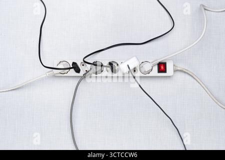 Top view of a power strip with on/off switch and various plugged-in plugs and cables on a white Resopal panel Stock Photo
