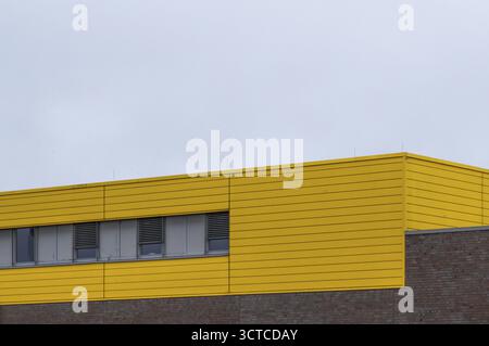 Modern building displaying a bright yellow facade with horizontal panels, windows, and a brick wall Stock Photo