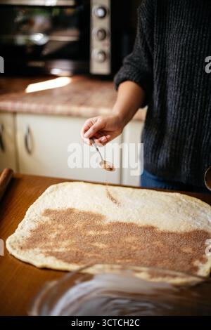Sprinkling cinnamon on rolled dough Stock Photo