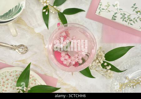 Sakura celebration: pink drink with delicate decorations. Top view table setting: drink in a glass, white and green decors: pearls, flowers and leaves. Stock Photo
