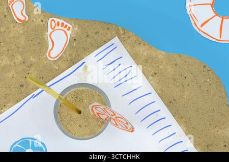Mixed media:photo combined with drawing. Untypical drink presentation on a beach. Instead of juice there is sand in a glass. Stock Photo