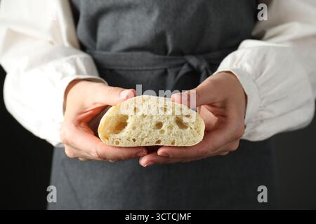 Woman holding half of fresh ciabatta on black background, closeup Stock Photo