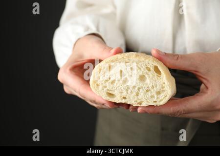 Woman holding half of fresh ciabatta on black background, closeup Stock Photo
