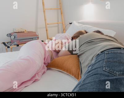 Man and woman resting on bed in hotel room with suitcase and soft light. Concept of travel, relaxation, and modern comfort Stock Photo