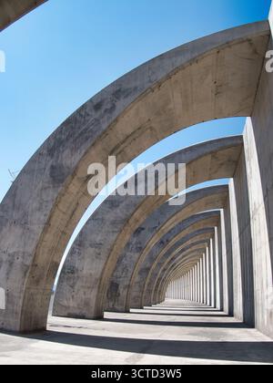 Contemporary Architectural Concrete Arches - Modern concrete structure of repeated curving arches under a bright blue sky, creating a rhythmic abstrac Stock Photo