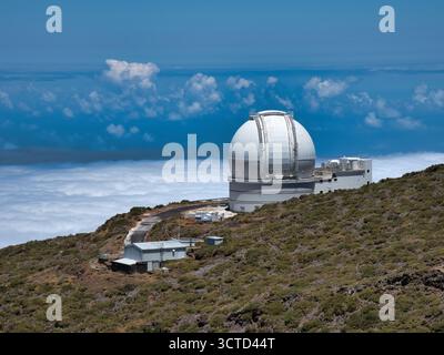 White Spherical Telescope Dome on Peak - Large white astronomical observatory with a spherical dome set high on a mountain ridge, overlooking clouds a Stock Photo
