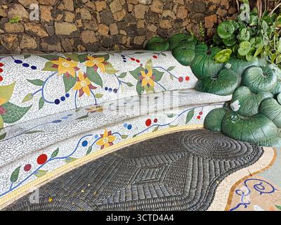 Artistic Mosaic Bench and Pebble Floor Detail - Decorative garden bench with ceramic mosaic and river stones forming a spiral floor pattern. Stock Photo