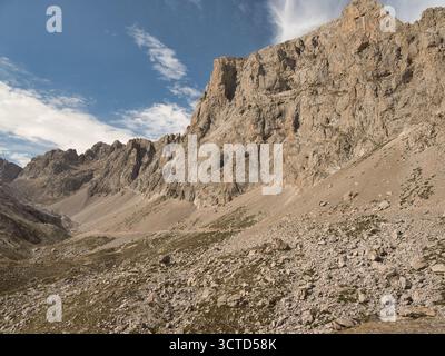 Towering sheer cliff face in misty gorge - Dramatic low-angle shot of a massive, vertical rock cliff with scree slopes disappearing into mist and fog Stock Photo