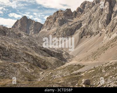 Towering sheer cliff face in misty gorge - Dramatic low-angle shot of a massive, vertical rock cliff with scree slopes disappearing into mist and fog Stock Photo