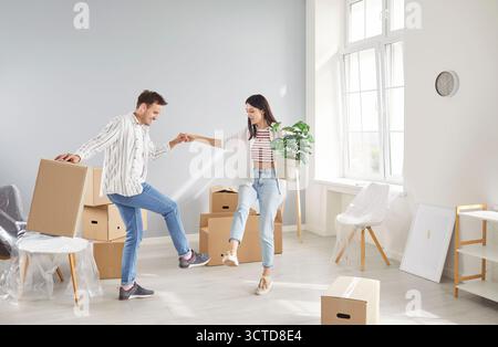 Happy young couple dancing together in their new home surrounded by boxes, having fun on moving day. Stock Photo