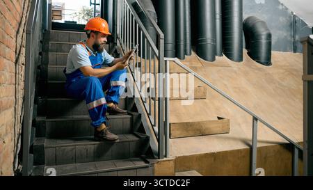 Technician using tablet on industrial staircase during break Stock Photo