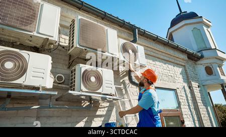 Technician inspecting outdoor air conditioning units under bright sunlight Stock Photo