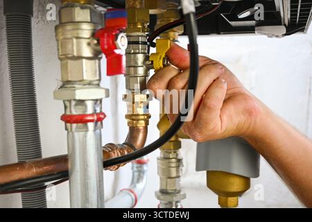 Hand turning a yellow valve on complex plumbing pipes in a boiler system. Stock Photo