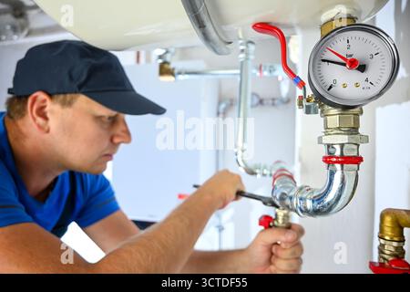 Plumber checking pressure gauge and adjusting pipes of a heating system. Stock Photo