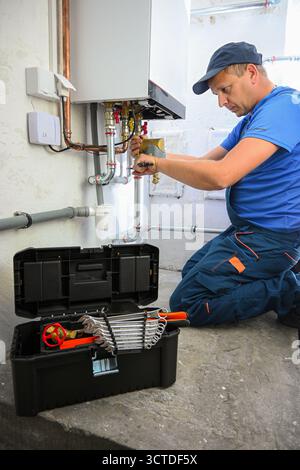 Plumber working on a heating boiler system, repairing pipes with a wrench and other tools. Stock Photo