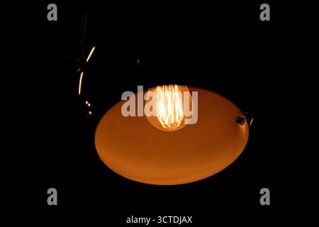 Glowing Edison Light Bulb in a Dark Industrial Lamp Stock Photo