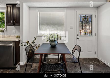 Small dining room with a black table and four chairs. A vase with flowers sits on the table Stock Photo
