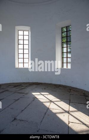 Sunlight entering through tall rectangular windows of an old white wall building, casting geometric shadows on stone floor. Minimalist architecture ba Stock Photo