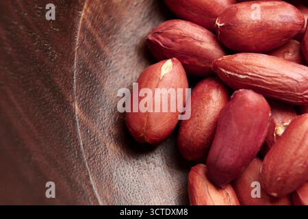 Roasted shelled peanuts in brown skin arranged in a wooden bowl. Macro. Stock Photo