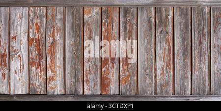 Old wooden wall made of grey weathered vertical boards with peeling orange paint Stock Photo