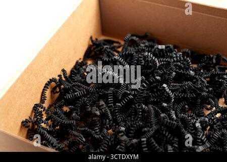 Open cardboard shipping box with black shredded paper filling. Fragile items packaging concept Stock Photo