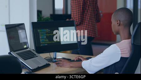 Coding female developer using laptop and external monitor in open-plan office, copy space Stock Photo