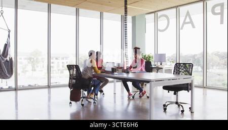 Collaborating three office workers using laptops in open-plan office, with hammock and coffee mugs Stock Photo