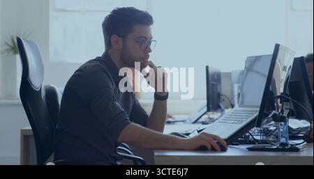 Man resting chin on hand using mouse at modern office desk, with laptop and external monitor Stock Photo