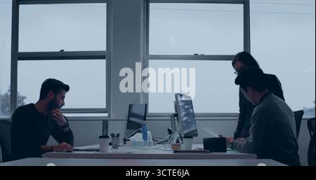 Collaborating professionals reviewing monitors and typing on laptop in office, with coffee cup Stock Photo