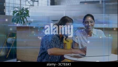 Collaborating coworkers reviewing data on silver laptop in office lounge, with overlays and tablet Stock Photo