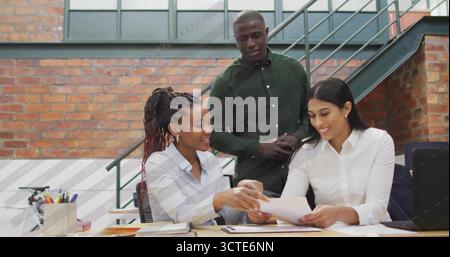 Collaborating business casual coworkers reviewing documents at desk in office, with laptop and pens Stock Photo