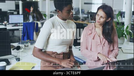 Two office colleagues working together at shared desk in open plan office, with laptop and tablet Stock Photo