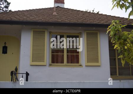 A quaint white house with pastel yellow shutters and brown shingle roof in California, USA, featuring a minimalist and cozy residential design. Stock Photo