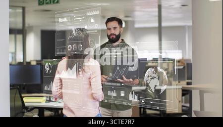 Two colleagues analyzing rotating charts in open office, with monitors and casual attire Stock Photo