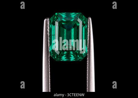 A green gemstone is being held up by a metal tool. The gemstone is large and shiny, and it is surrounded by a clear plastic case. Concept of wonder an Stock Photo