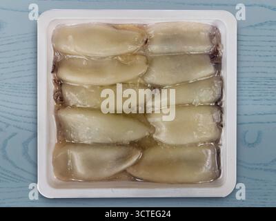 Vacuum-sealed frozen squid in plastic tray isolated on blue wood background, clipping path included Stock Photo