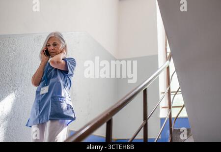 Tired nurse taking break during hospital shift, calling with family. Stock Photo