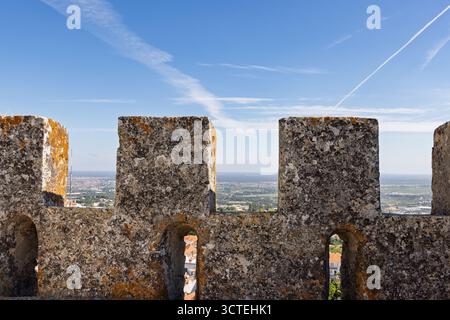 View of the distant plains and clear blue sky framed by the weathered, moss-covered battlements of Palmela Castle in Portugal. Stock Photo