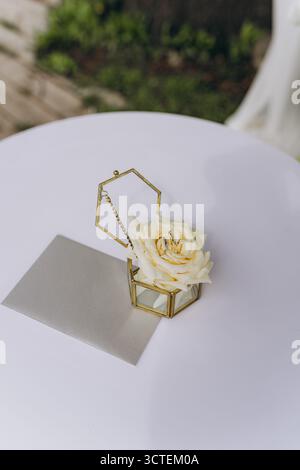 A charming display of a yellow rose nestled in a decorative gold geometric box alongside wedding rings and a silver envelope resting invitingly on a c Stock Photo