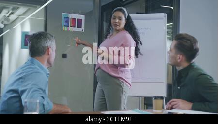 Pointing pregnant woman wearing pink top explaining phone mockups on whiteboard in conference room Stock Photo