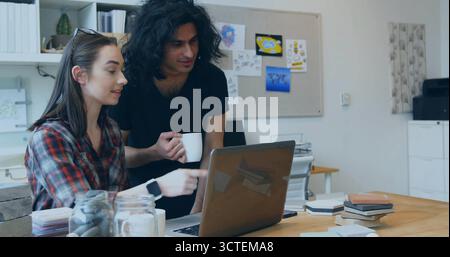 Collaborating team focusing on laptop screen at design studio desk, with coffee mug and sketches Stock Photo