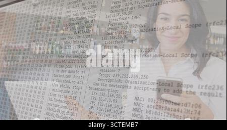 Working IT professional holding smartphone and typing on laptop at office desk, with code overlay Stock Photo