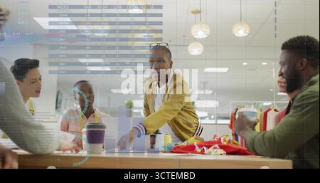 Collaborating six designers leaning over wooden worktable in studio, with swatches, tape measures Stock Photo
