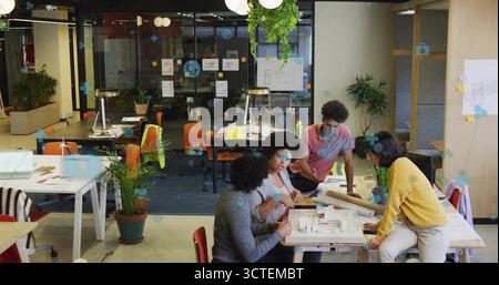 Collaborating four designers analyzing scale model in open-plan office, with blueprints and pens Stock Photo