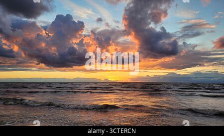 A dramatic and majestic sunset over the Baltic Sea on the coast of Latvia. The sky erupts in a fiery display of orange, yellow, and purple. Stock Photo