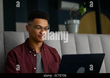 Focused young man in smart casual and eyeglasses using laptop in office Stock Photo
